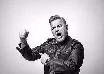 Moderátor v tmavé košili gestikuluje během prezentace na světlém pozadí.