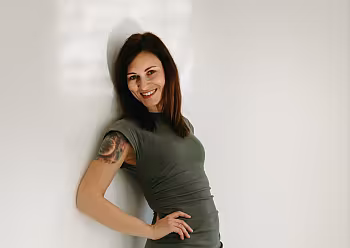 Michaela Casková v zelených šatech opřená o bílou zeď.