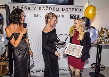 Moderátorka v černém vede rozhovor s ženou v růžových šatech při společenské události.
