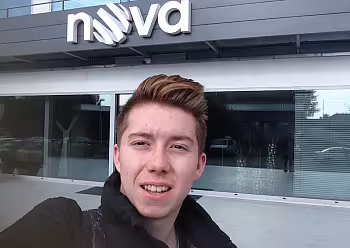 Moderátor v černém oblečení před moderní budovou s logem Nova.